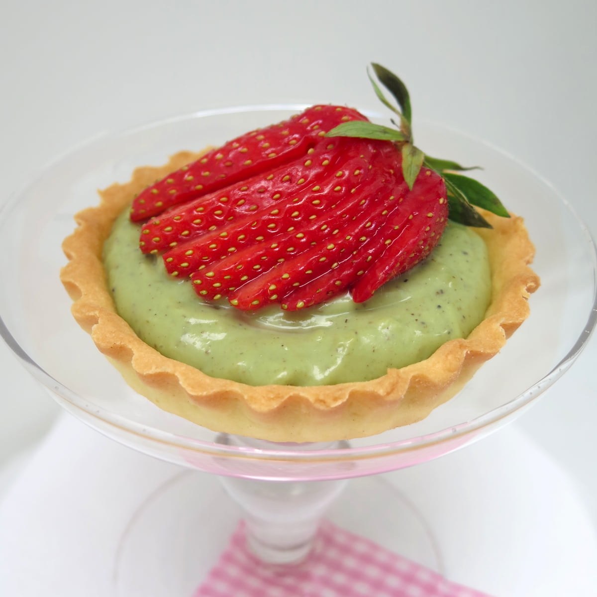 strawberry tart and pistachio cream (egg yolk recipe) glass dish holding a tart with green pistachio cream topped with a fanned strawberry