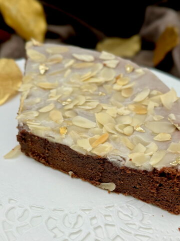 a large slice of chocolate cake topped with a rum glaze, toasted flaked almonds and gold leaf