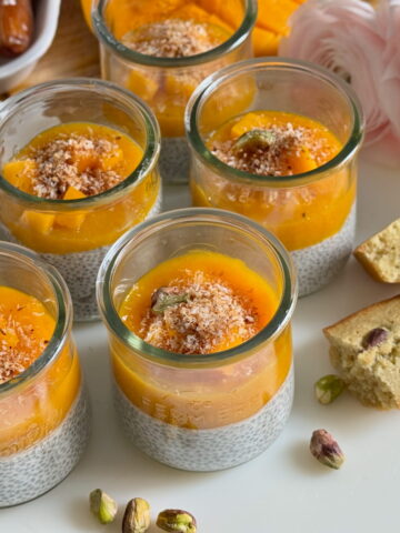 glass pots with coconut chia pudding topped with mango sauce, mango chunks and dates
